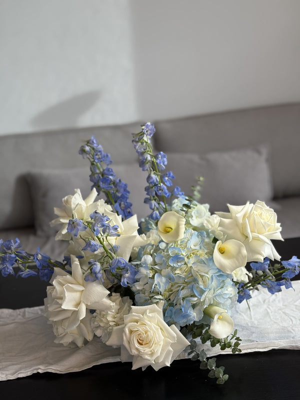 Bouquet of white and blue flowers on a table with a gray couch in the background