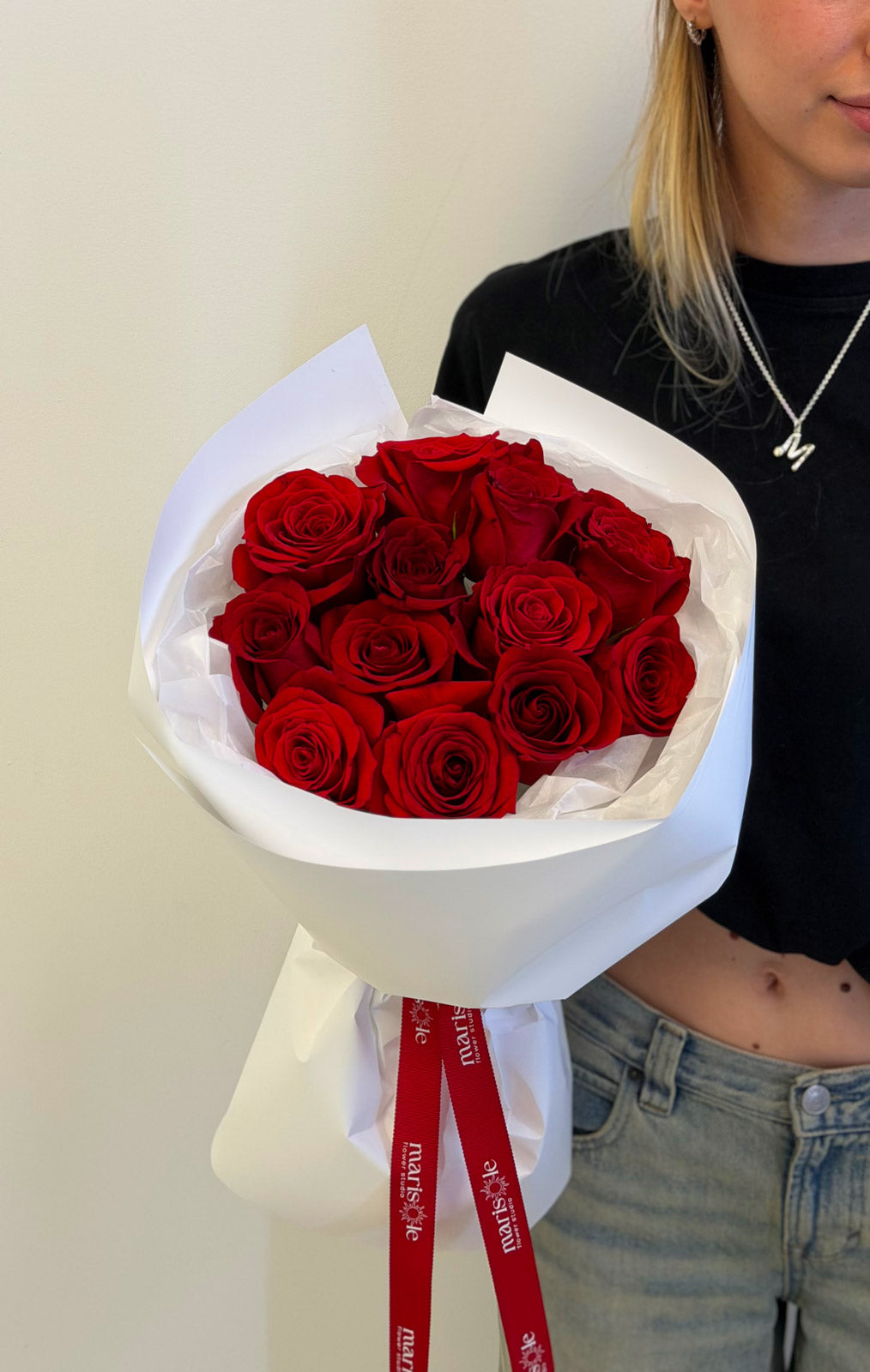 Person holding a bouquet of red roses wrapped in white paper with a visible brand label.