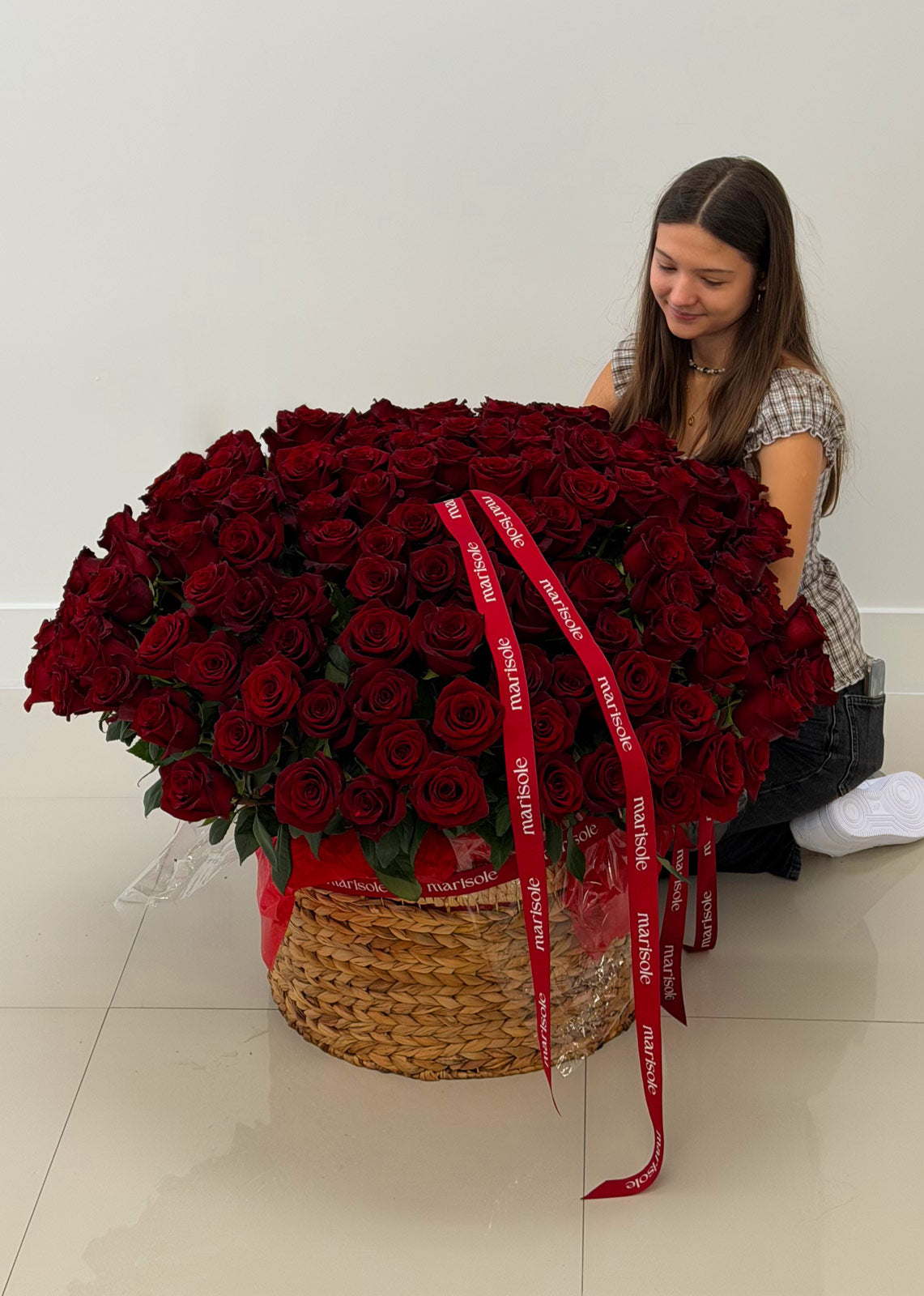 Person holding a large bouquet of red roses with a visible brand name on the ribbon.