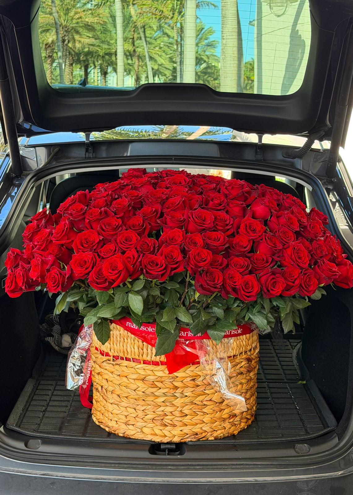 Basket of red roses in a car trunk with palm trees in the background