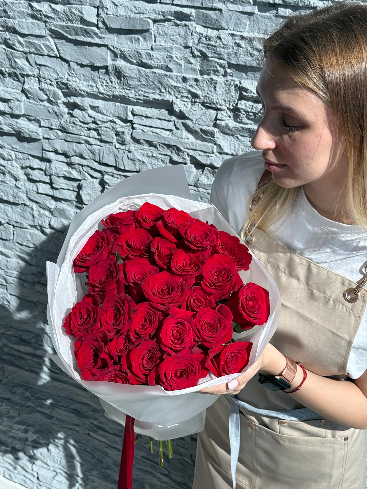 Person holding a large bouquet of red roses against a stone wall.