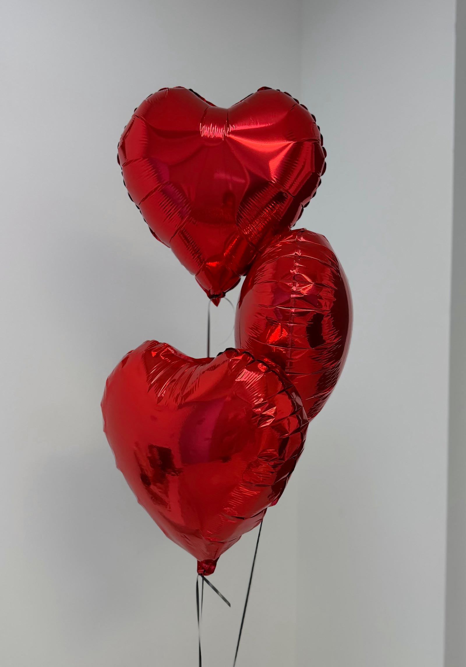 Three red heart-shaped balloons on a light gray background