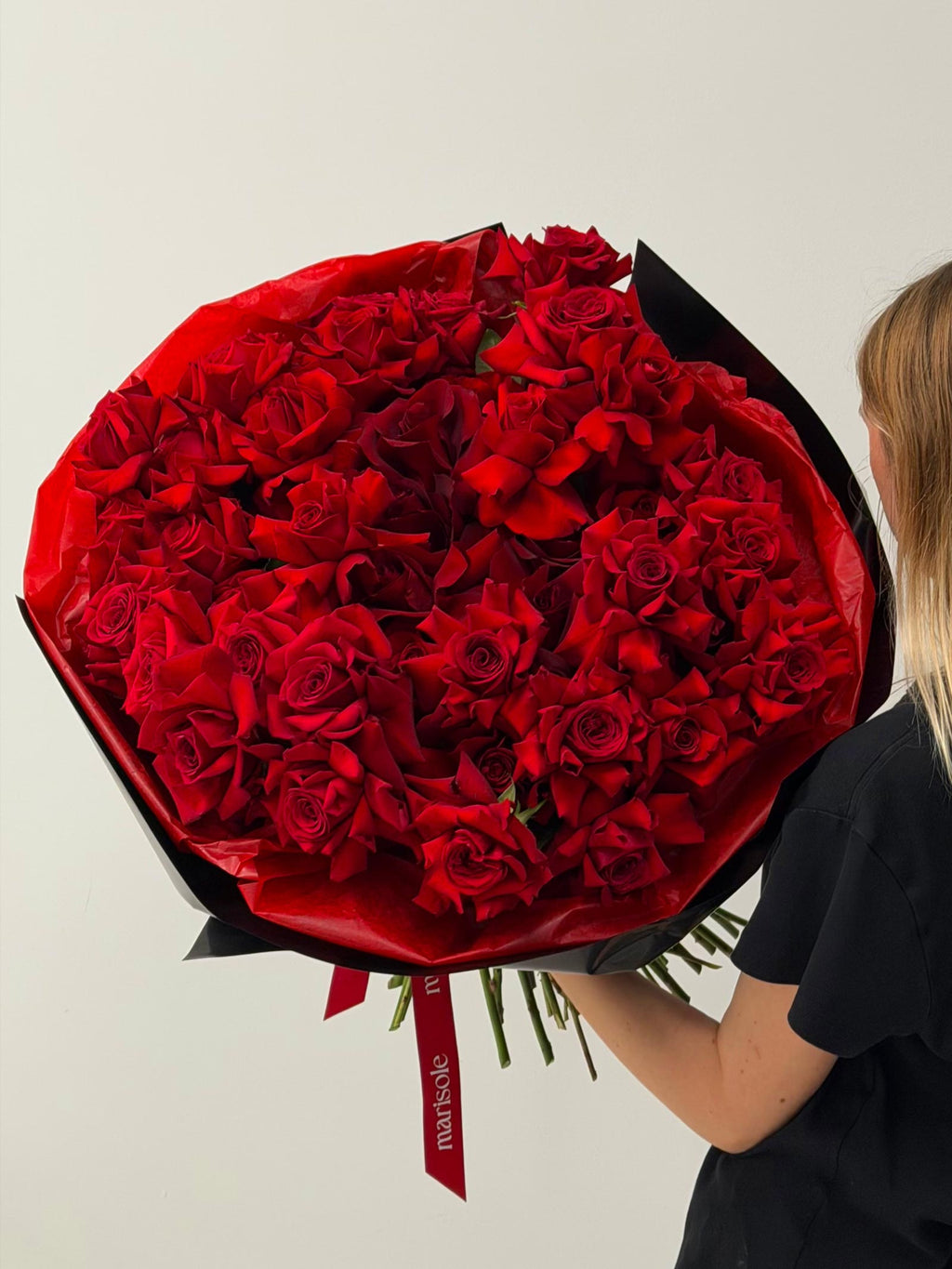 Person holding a large bouquet of red roses against a plain background
