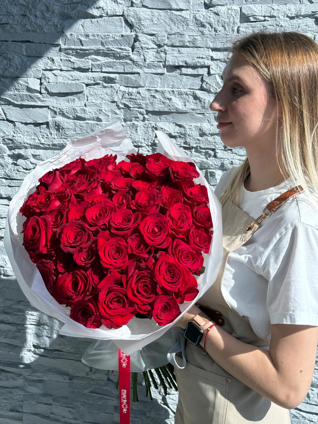 Woman holding a large bouquet of red roses against a stone wall.