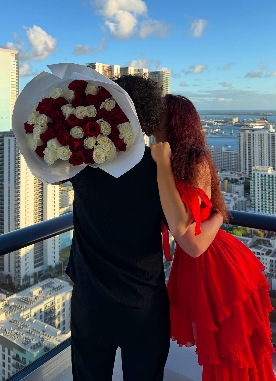 Couple on a rooftop with a large bouquet of red and white roses, city skyline in the background