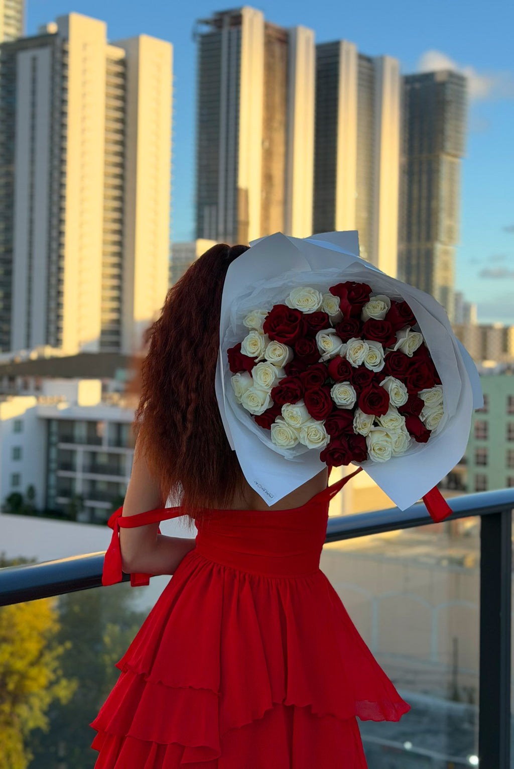 Person in a red dress holding a large bouquet of flowers with city skyline in the background