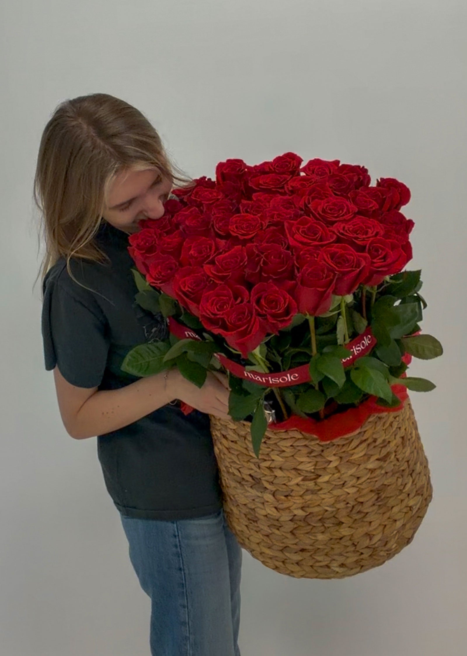 Person holding a large bouquet of red roses in a woven basket against a plain background