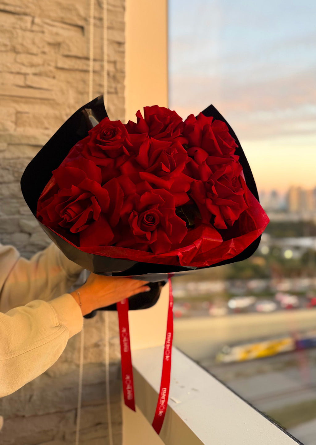 Bouquet of red roses held by a person with a cityscape in the background