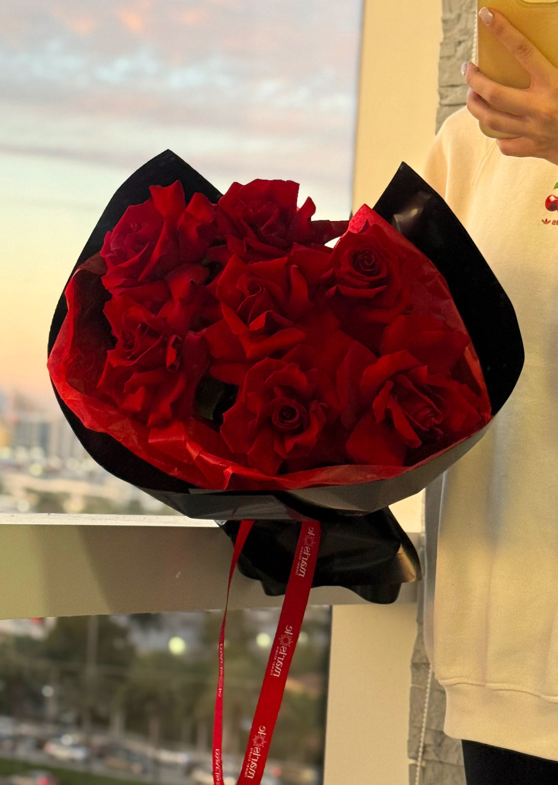 Bouquet of red roses wrapped in black paper with a red ribbon held by a person.
