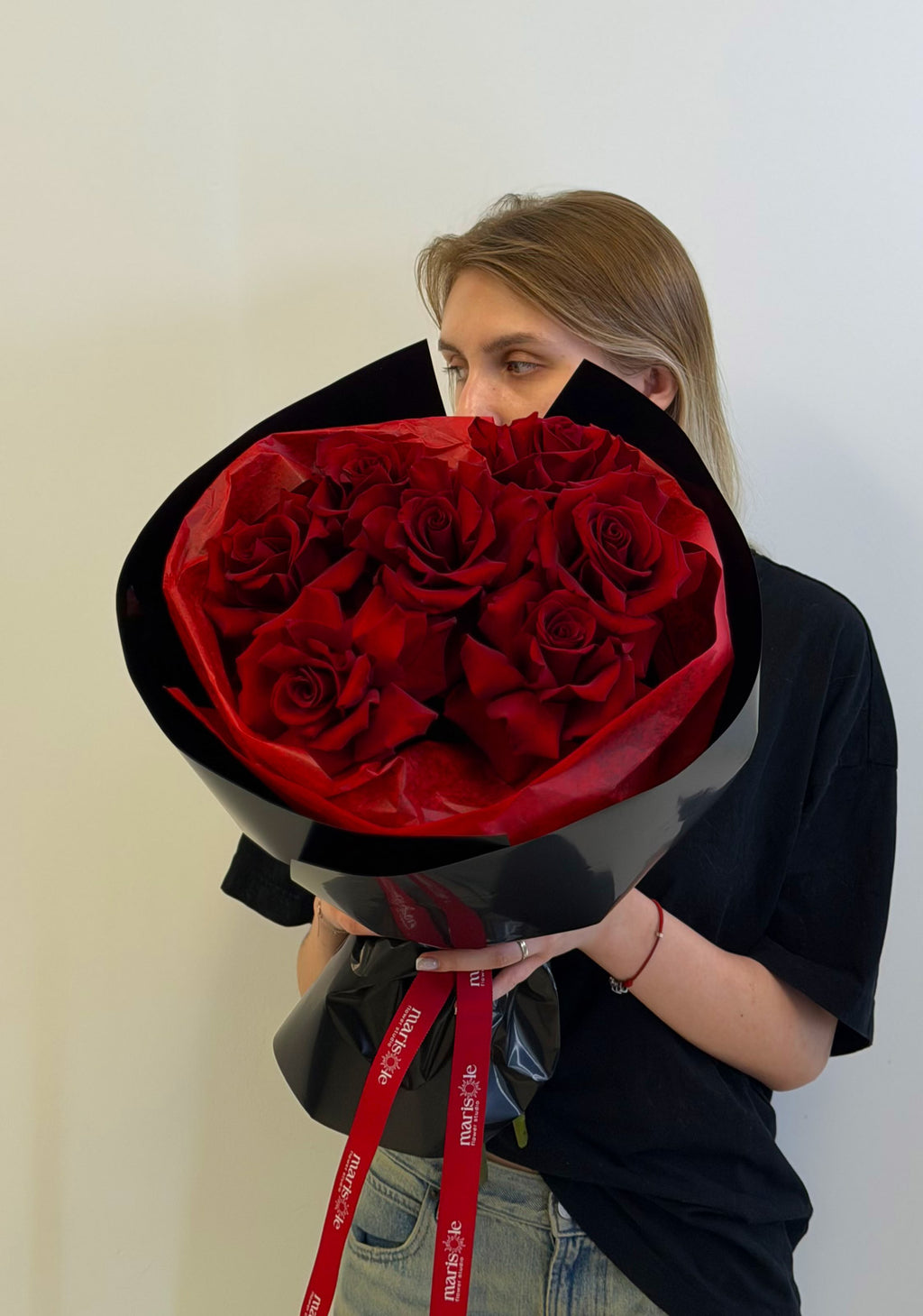 Person holding a large bouquet of red roses wrapped in black paper with a red ribbon.