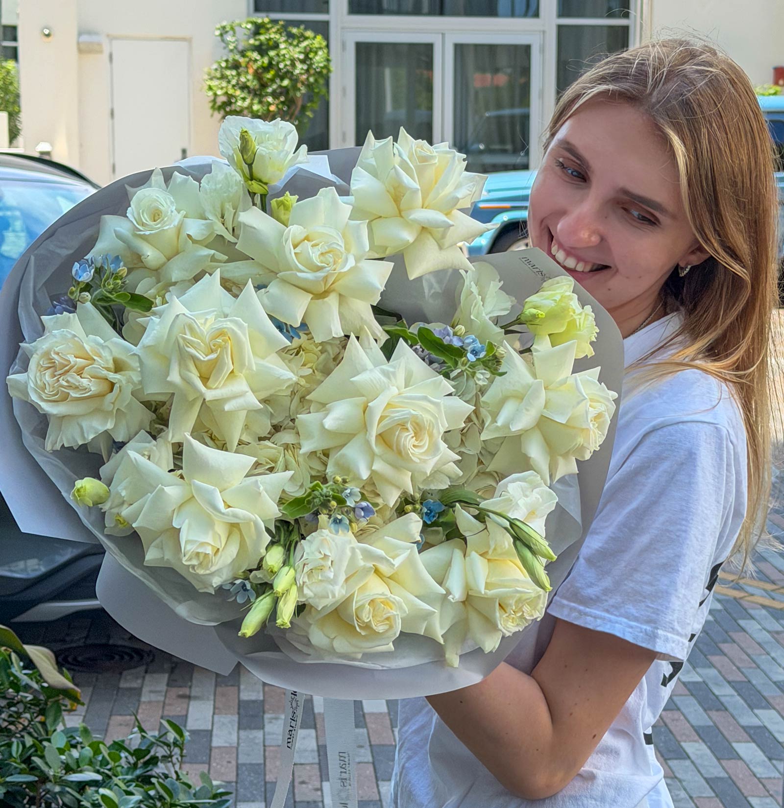 Woman holding a large bouquet of white flowers outdoors.