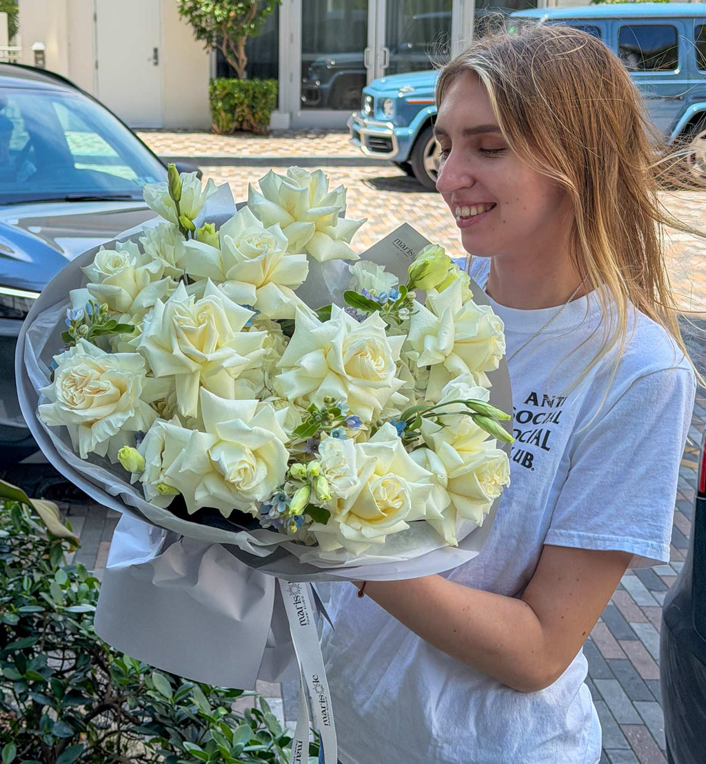 Woman holding a bouquet of white flowers outdoors with cars and a building in the background.