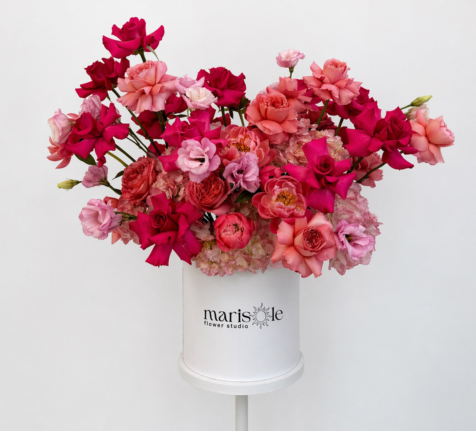 Bouquet of pink and red flowers in a white container with 'Marisole Flower Studio' branding on a white background.