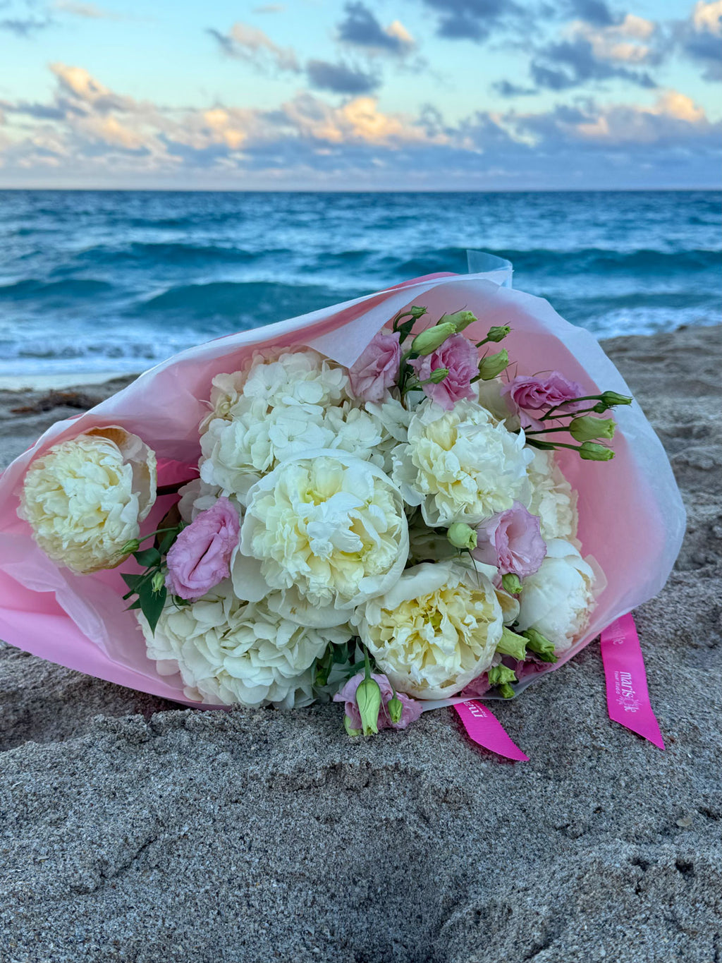 Bouquet of white and pink flowers on a sandy beach with ocean and sky in the background