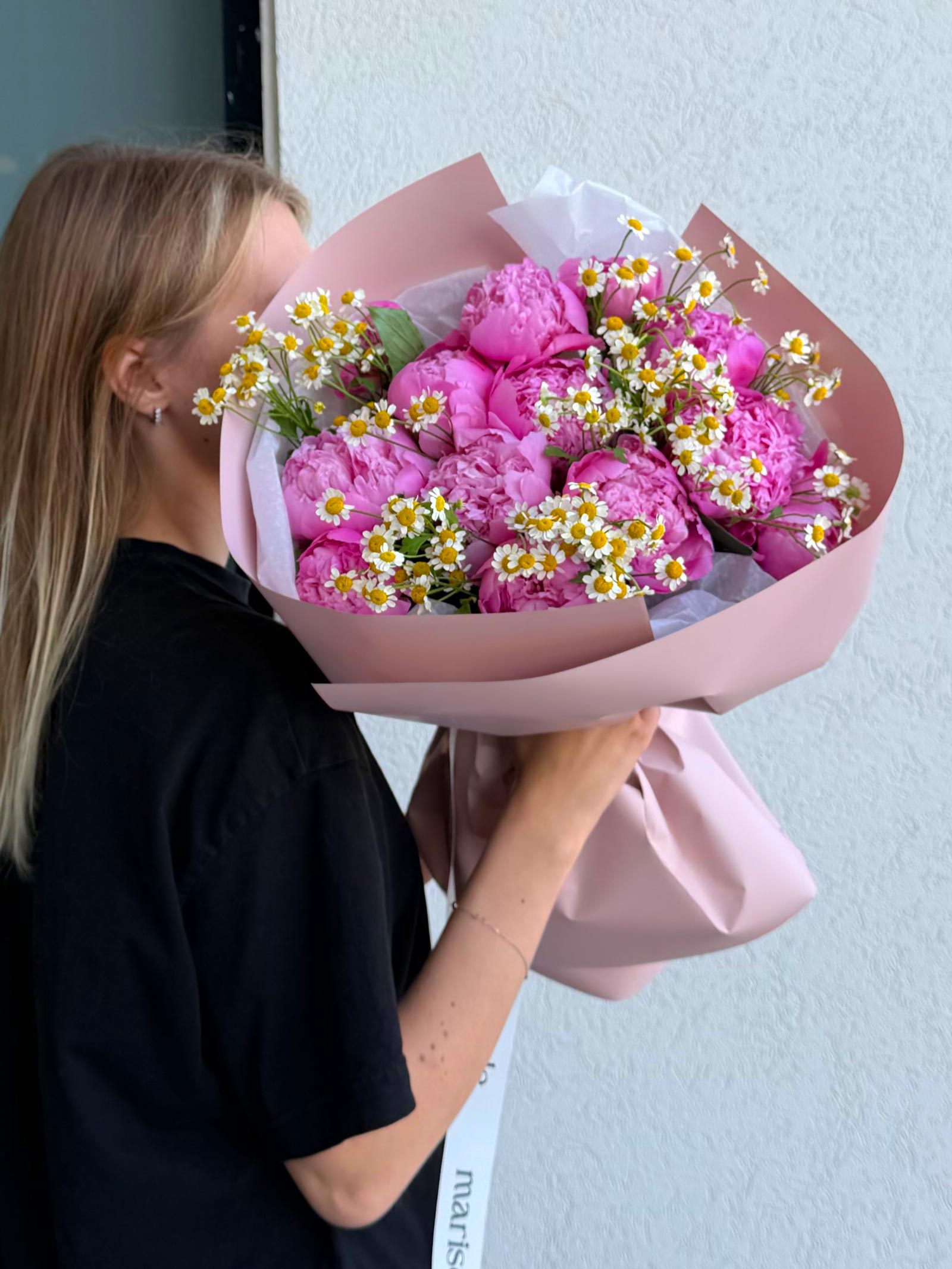 Person holding a bouquet of pink flowers with white accents against a light blue wall.