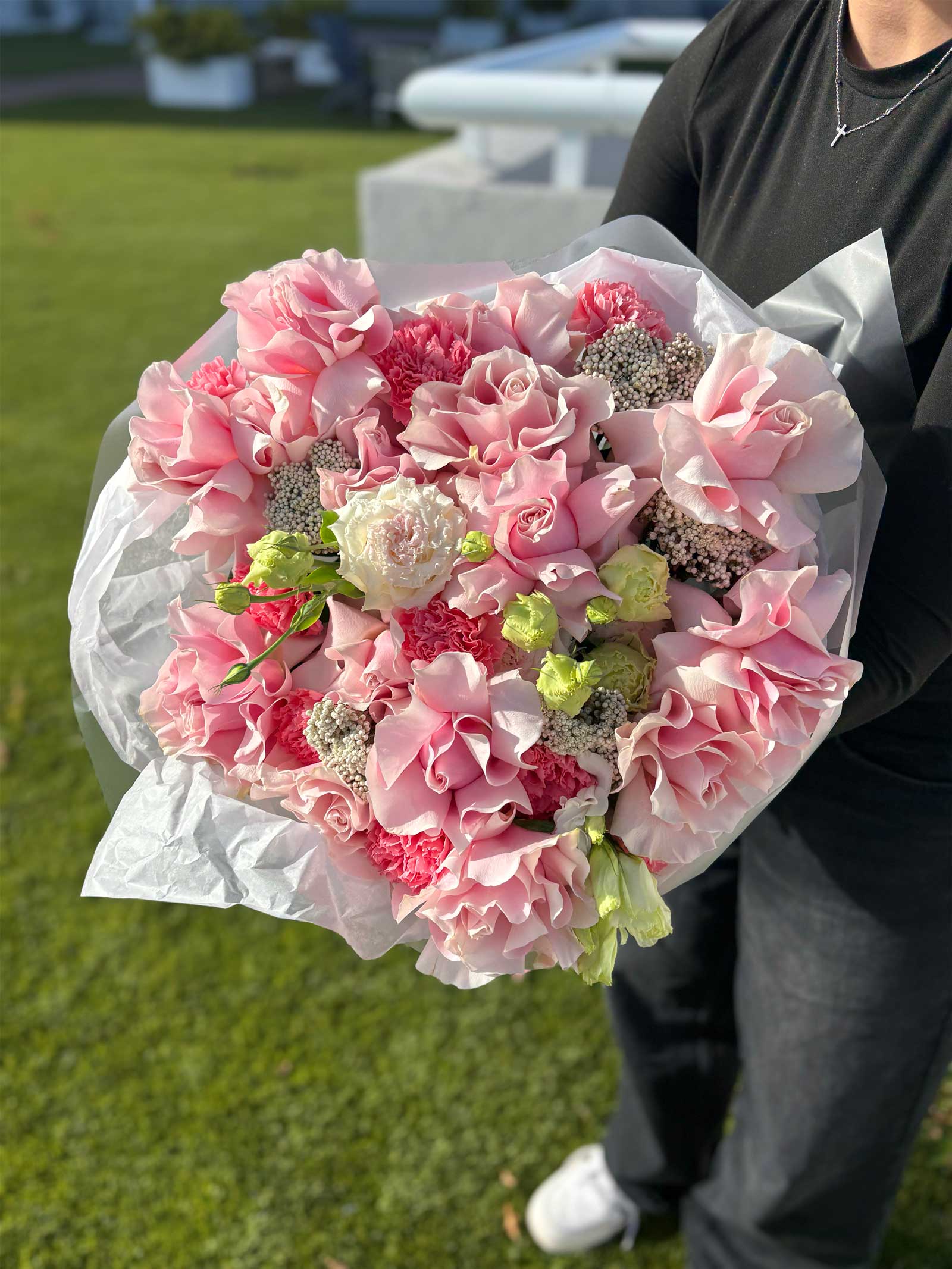 Person holding a bouquet of pink flowers outdoors on grass