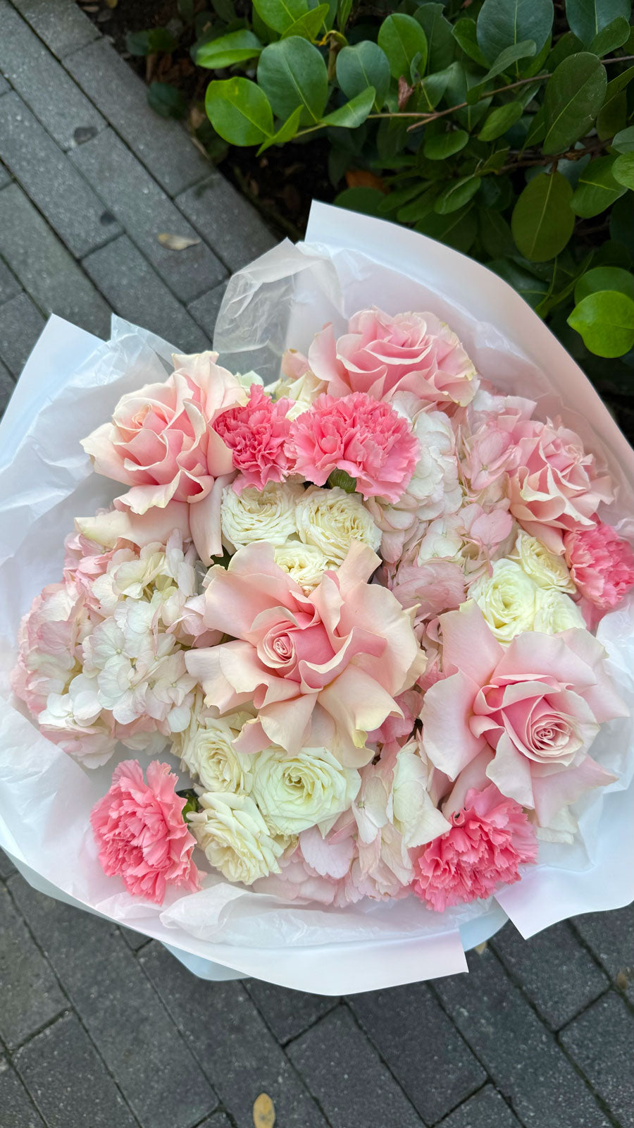 Bouquet of pink and white flowers on a gray pavement with greenery in the background