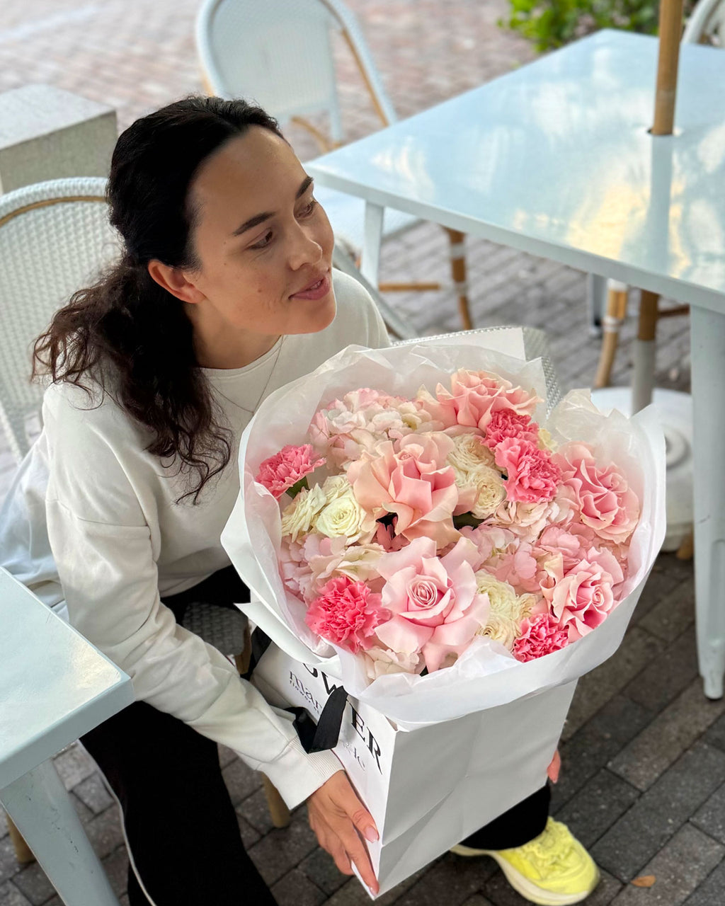 Woman holding a large bouquet of pink flowers outdoors.