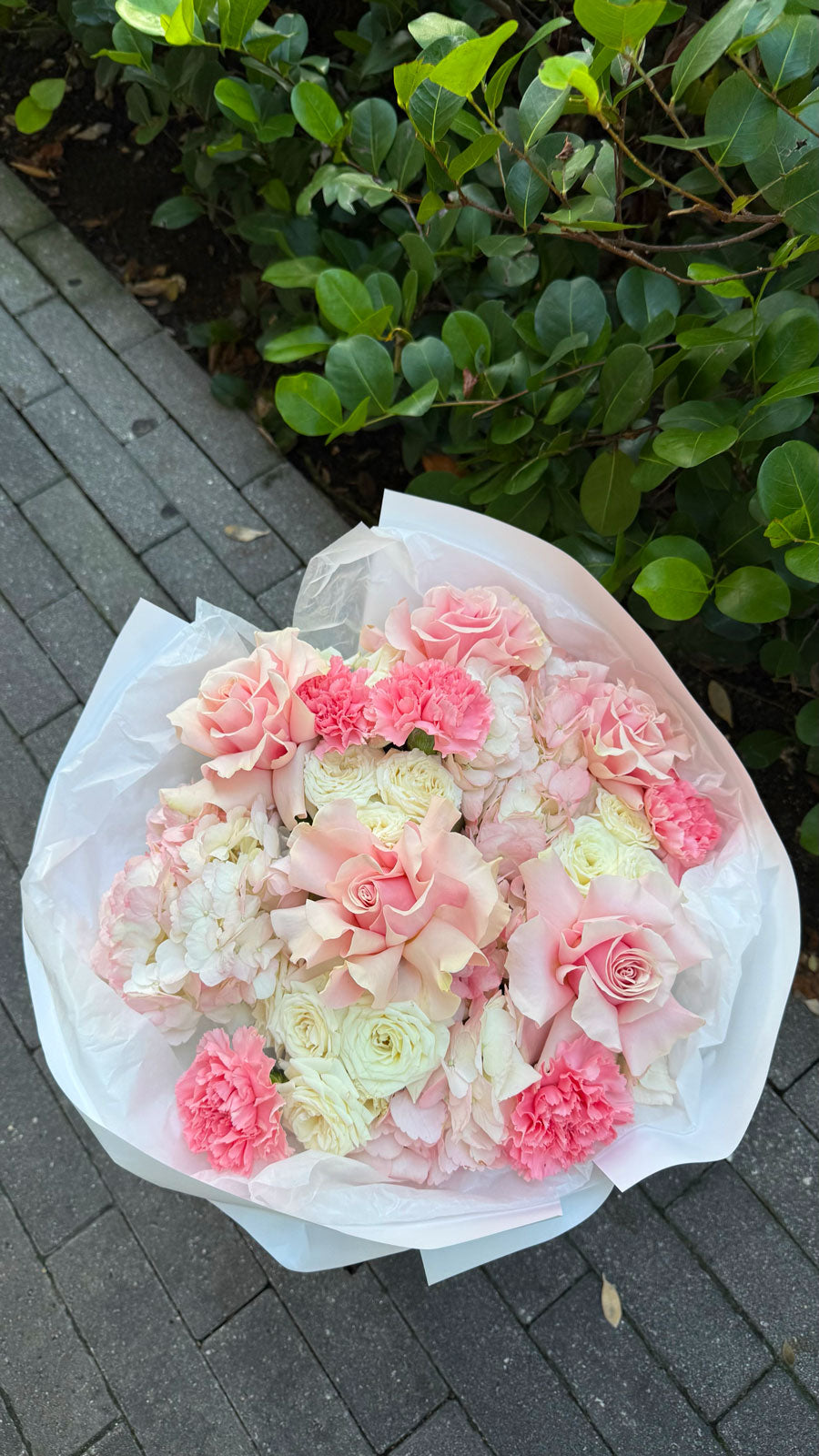 Bouquet of pink and white flowers on a paved surface with greenery in the background