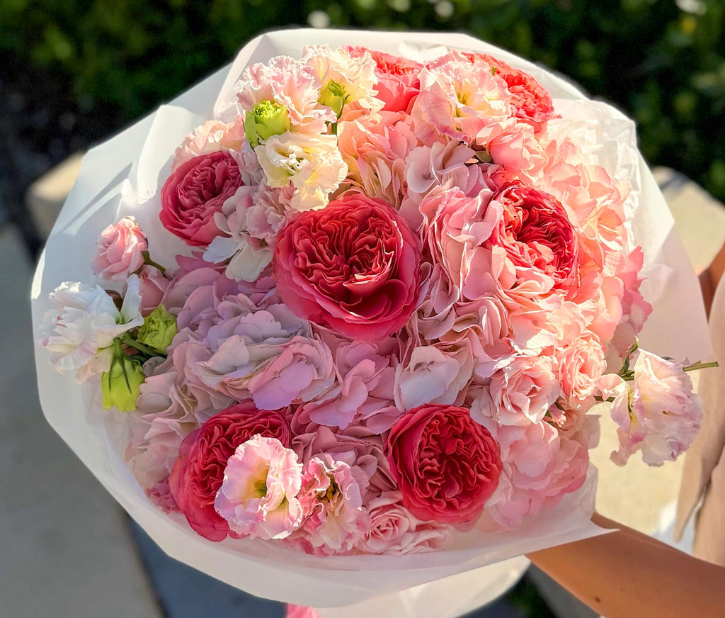 Bouquet of pink and red flowers held by a person outdoors.