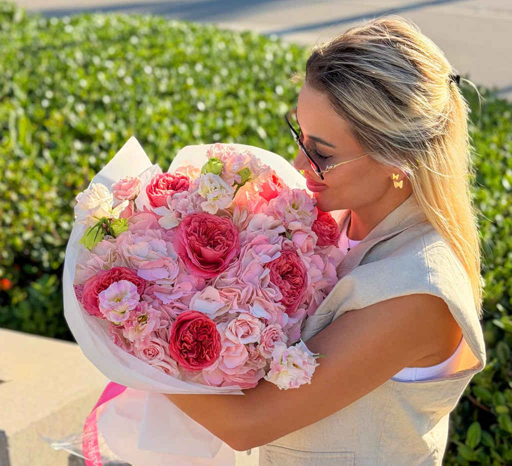Woman holding a large bouquet of pink flowers outdoors.