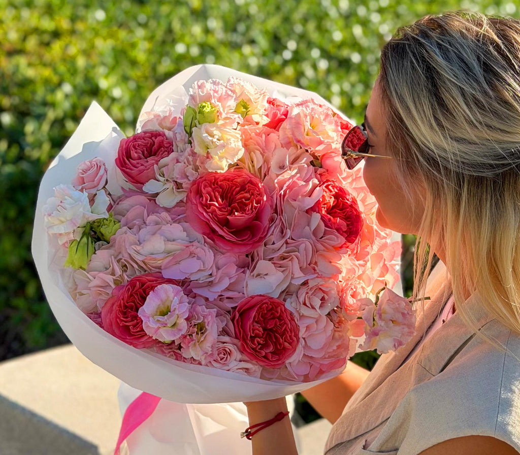 Woman holding a large bouquet of pink and red flowers outdoors.