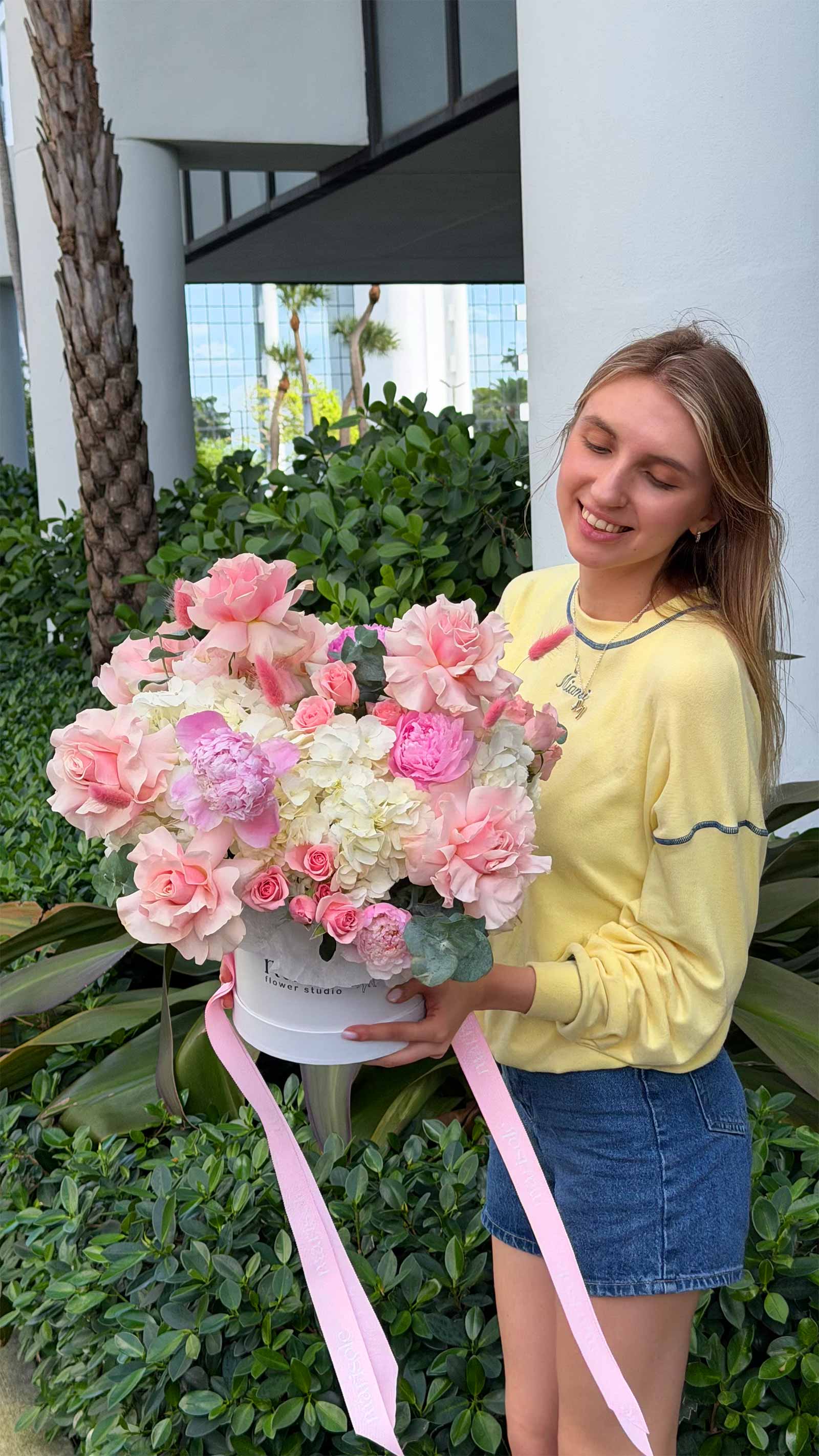 Woman holding a large bouquet of pink and white flowers with a pink ribbon.