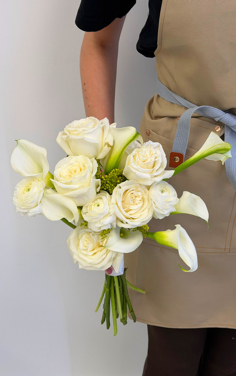 Bouquet of white roses and calla lilies held by a person wearing a beige apron.