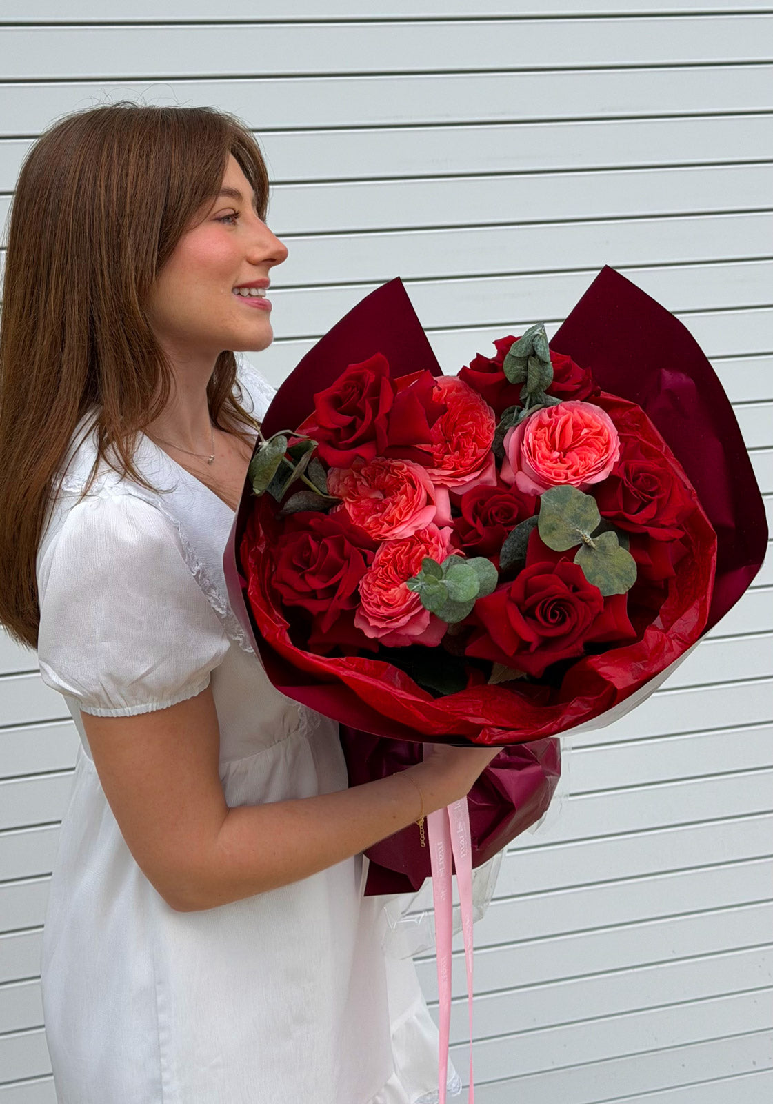 Woman holding a bouquet of red and pink roses against a light wooden background
