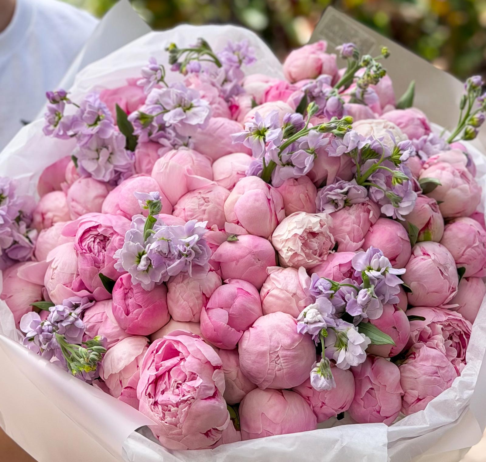 Bouquet of pink peonies with purple flowers in a white paper wrap.