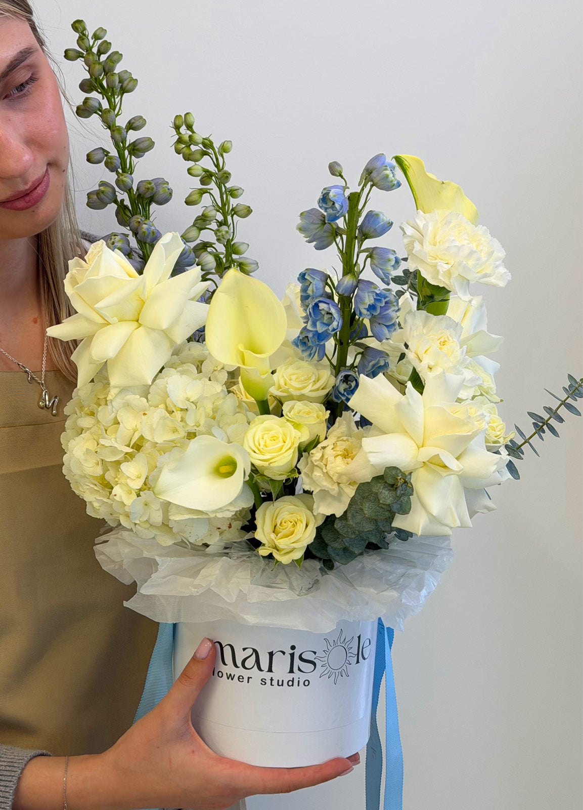 Person holding a bouquet of flowers in a white box with 'Marisole Flowers' branding