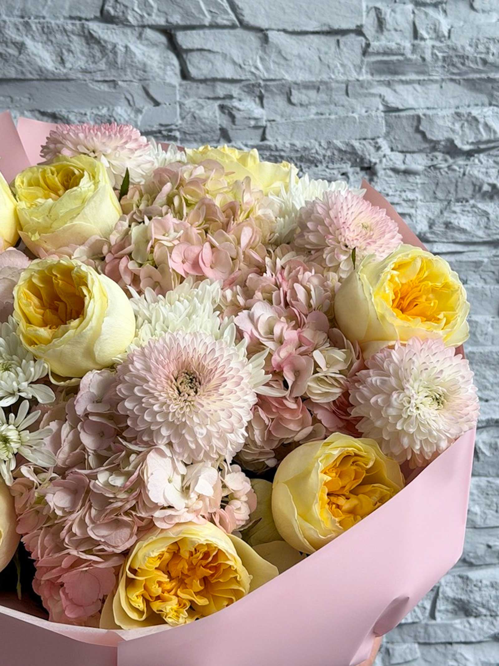 Bouquet of pink and yellow flowers in a pink wrap against a stone wall background