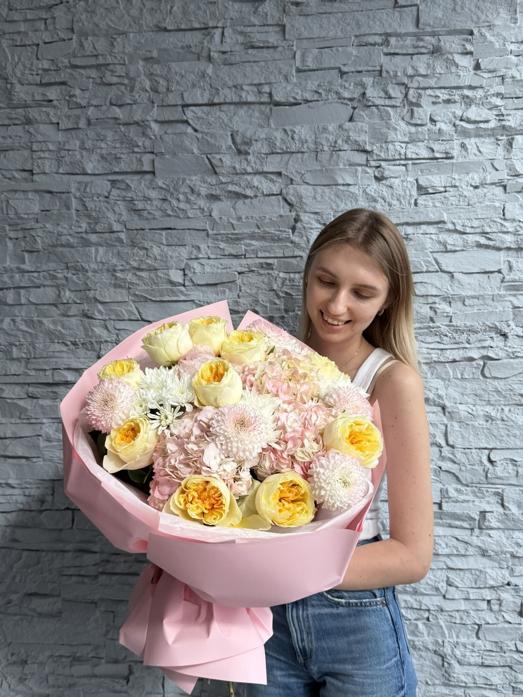 Woman holding a large bouquet of flowers against a gray stone wall.