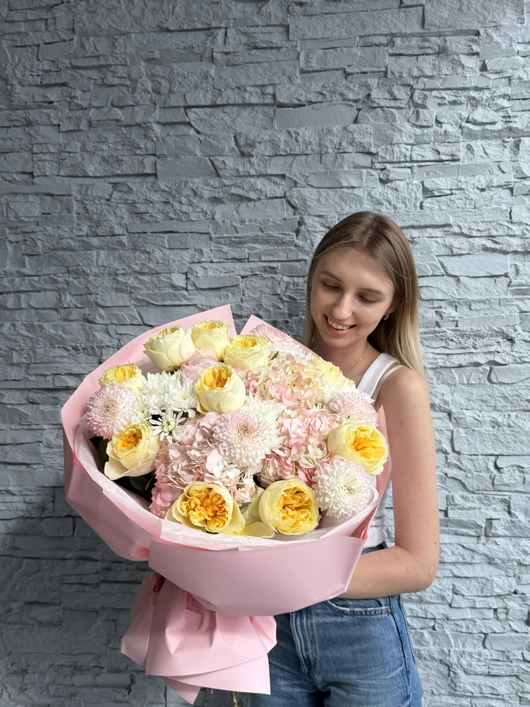 Woman holding a large bouquet of flowers against a gray stone wall.
