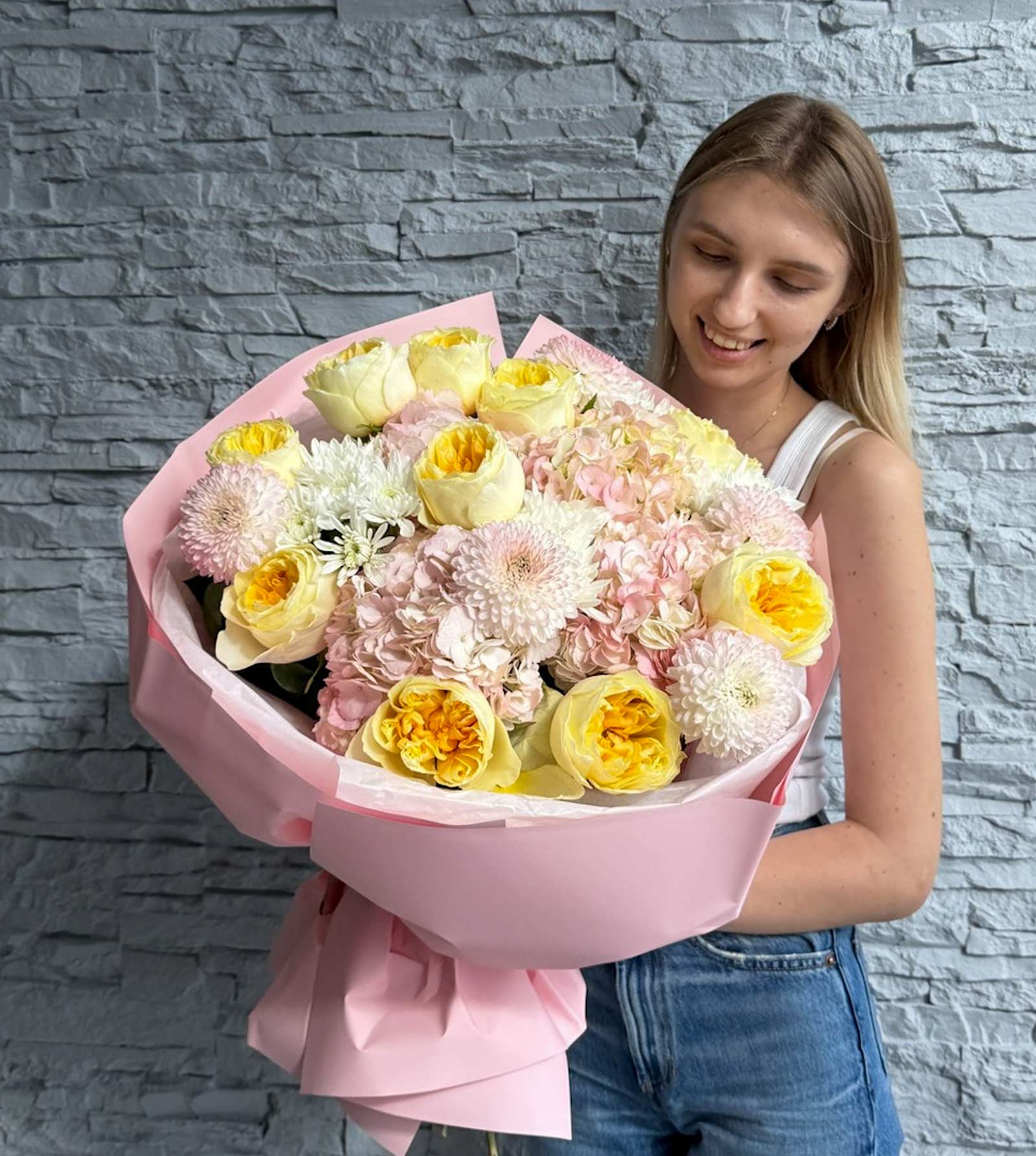 Woman holding a large bouquet of flowers against a stone wall.
