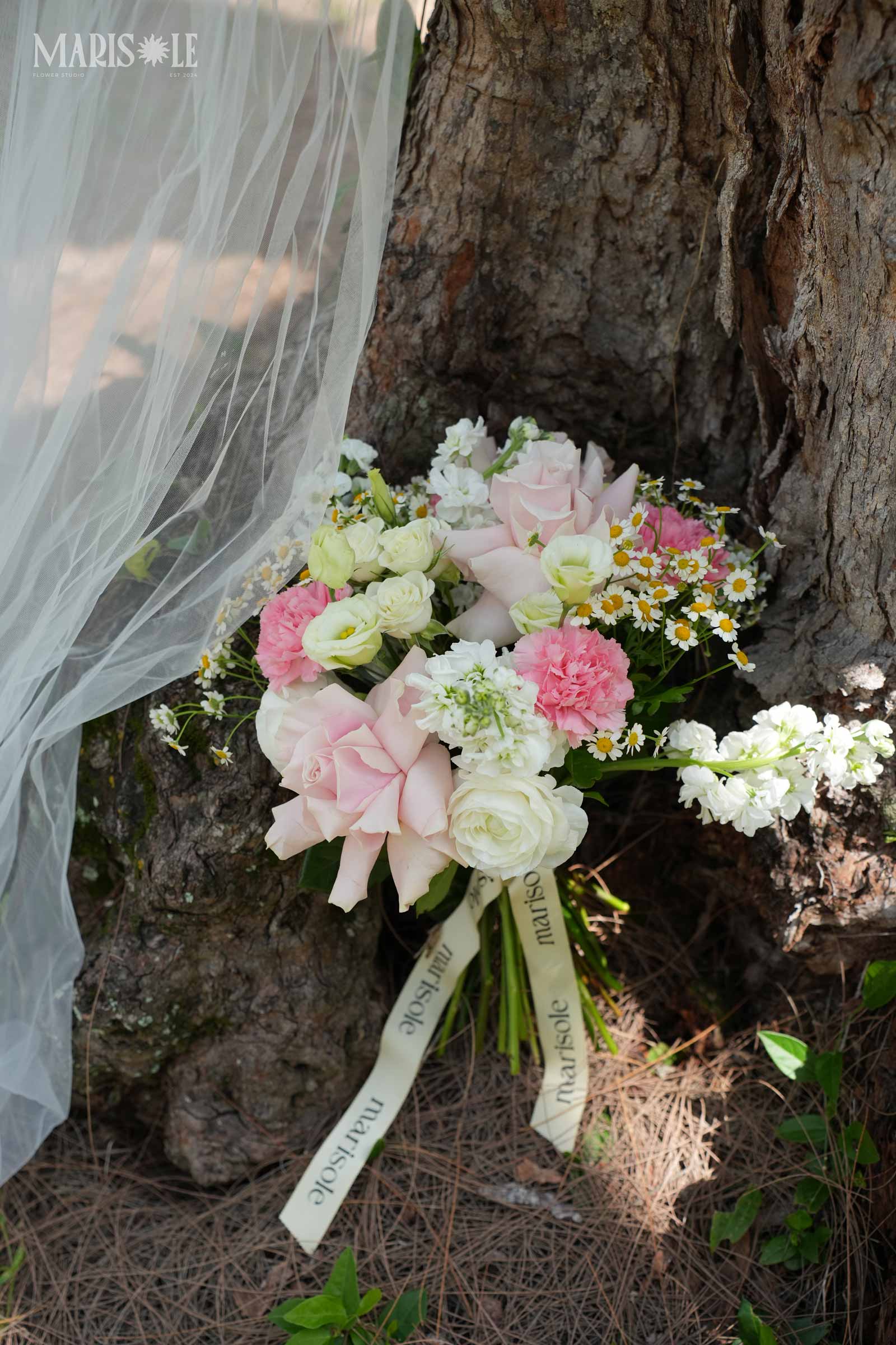 Pink and white bridal bouquet resting beside a tree with sheer fabric
