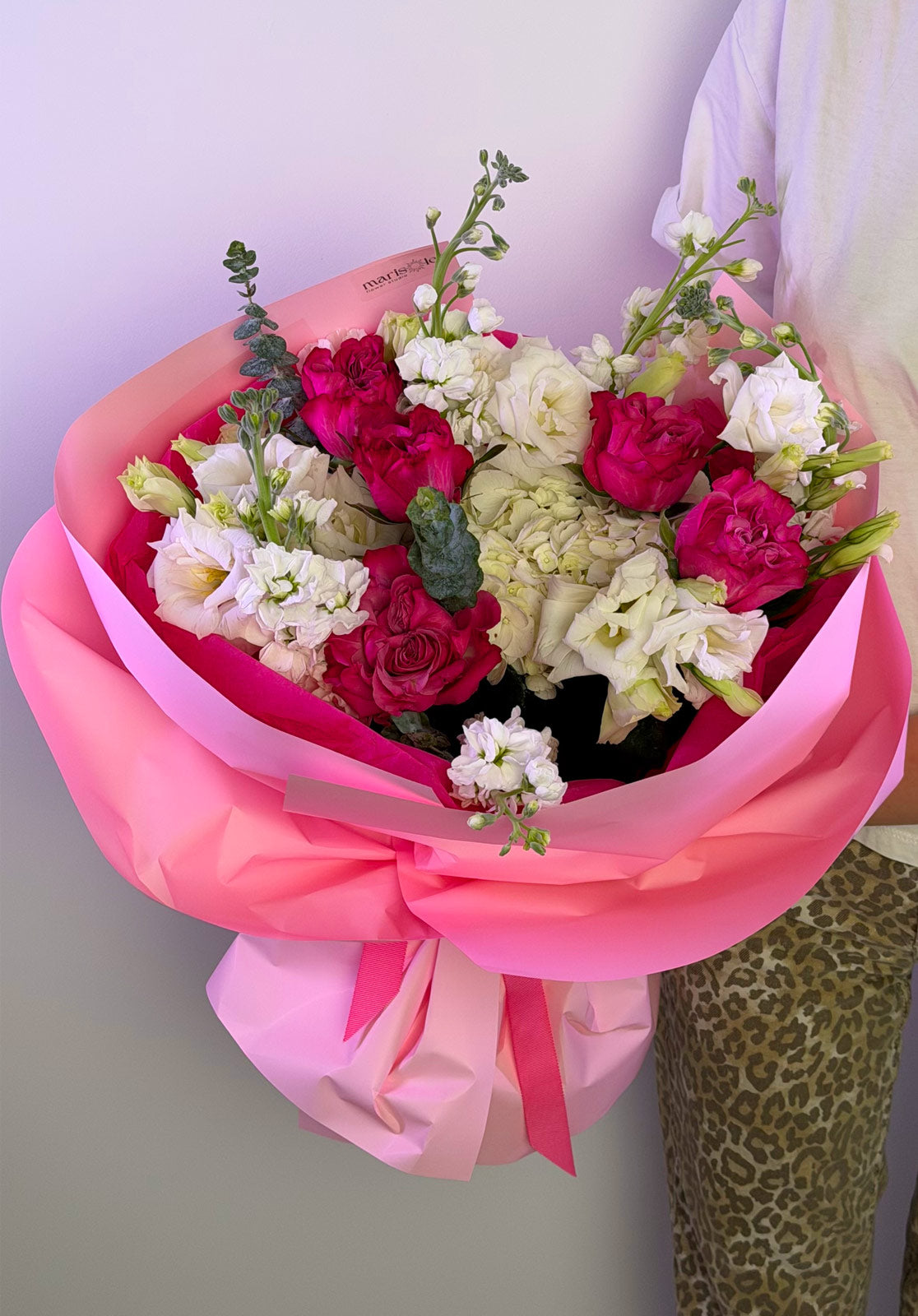 Bouquet of flowers wrapped in pink paper held by a person with a light background