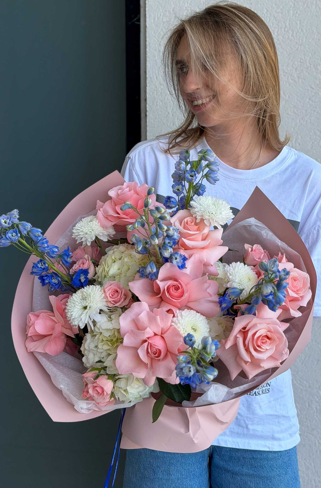 Woman holding Blush & Sky Bouquet with hydrangea, French roses, delphinium, spray roses, and chrysanthemums.