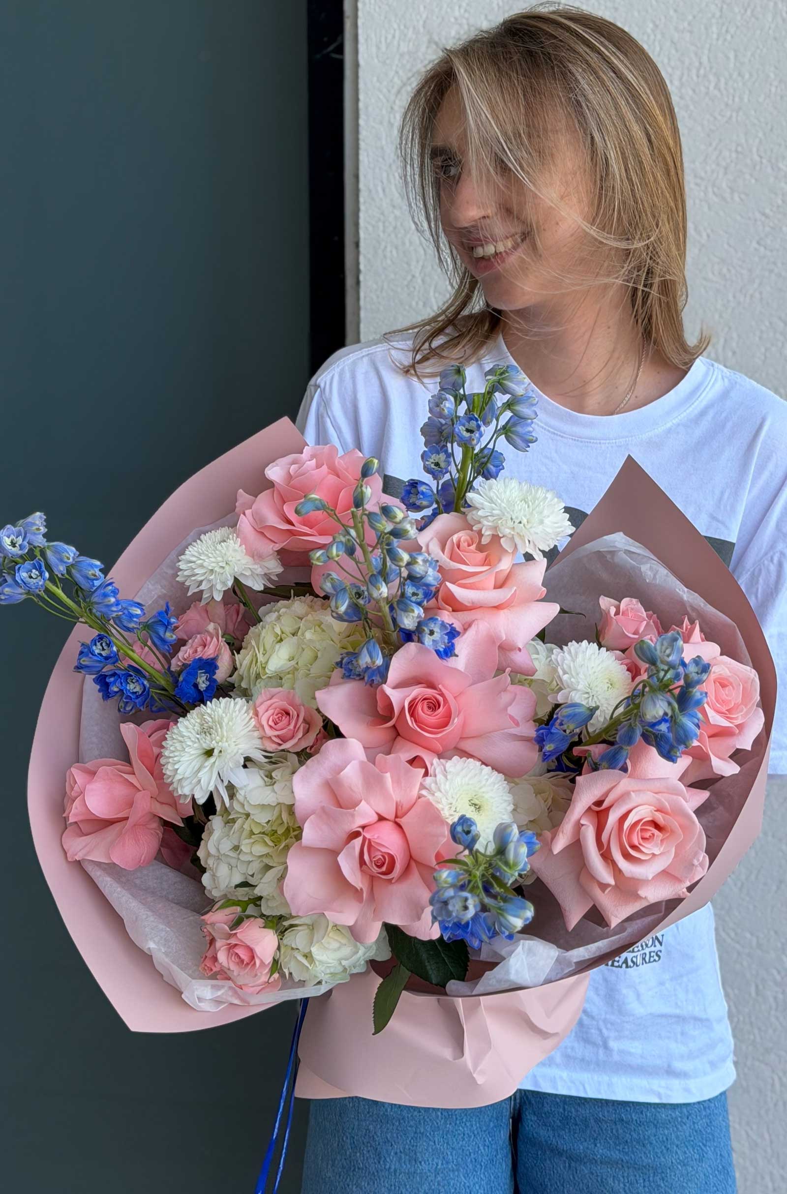 Woman holding Blush & Sky Bouquet with hydrangea, French roses, delphinium, spray roses, and chrysanthemums.