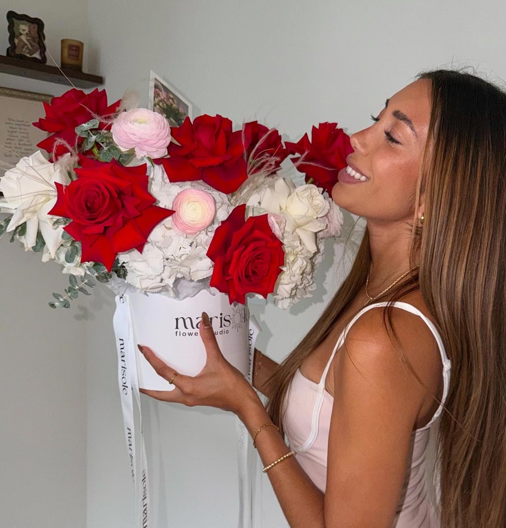 Woman holding a bouquet of red and white roses with a Marisole Flowers brand name.