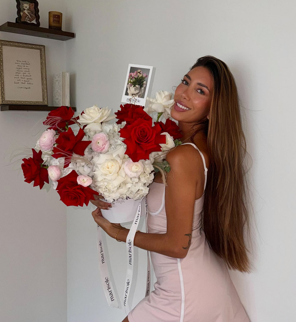 Woman holding a bouquet of red, white, and pink flowers against a light gray wall.
