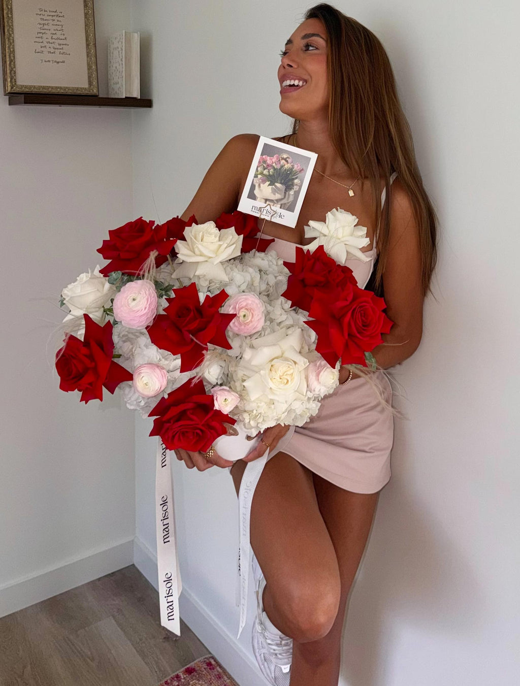 Woman holding a large bouquet of red, white, and pink flowers against a plain wall.