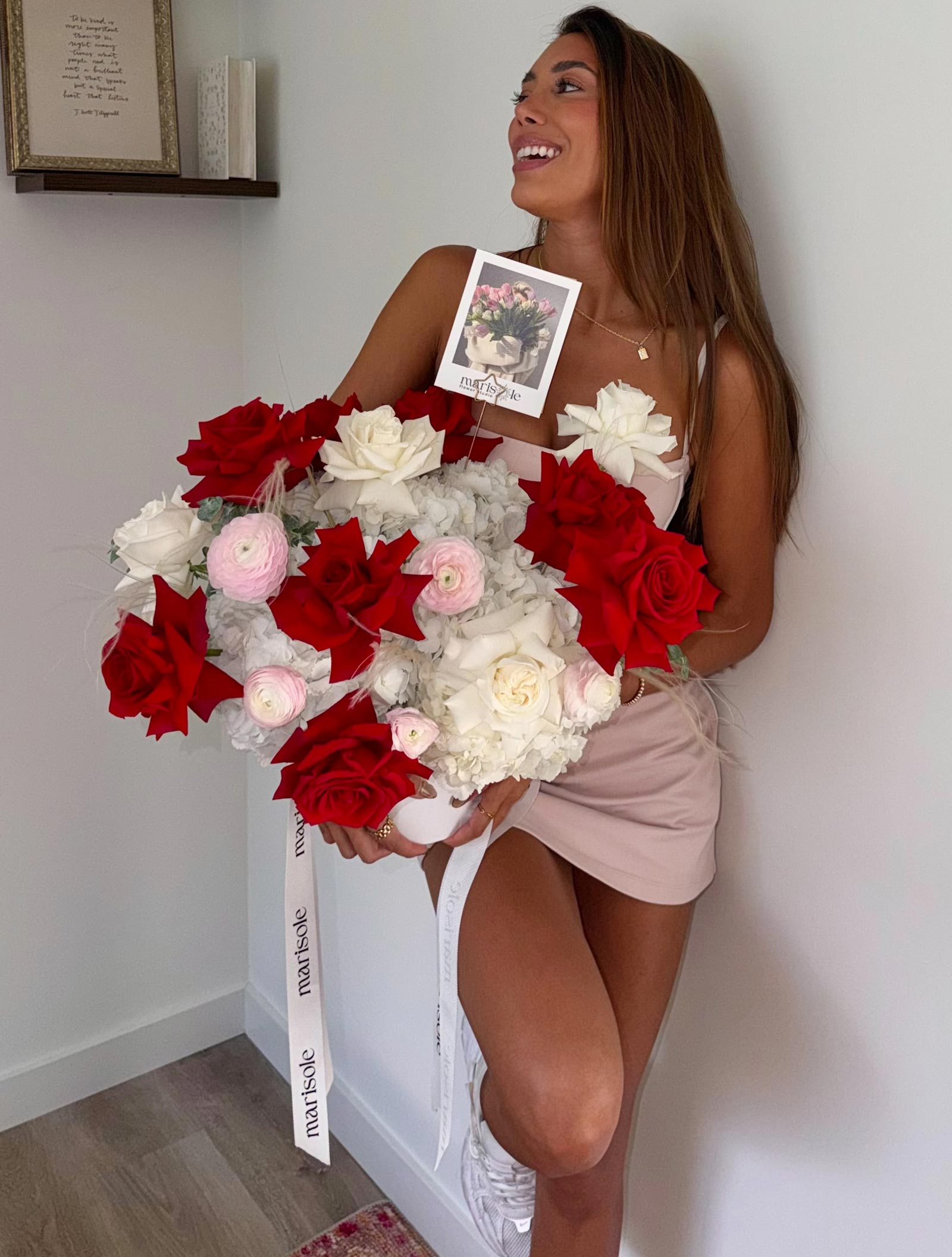 Woman holding a large bouquet of red, white, and pink flowers against a plain wall.