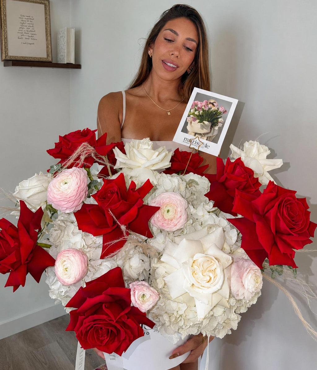 Woman holding a large bouquet of red, white, and pink flowers with a card in the background.