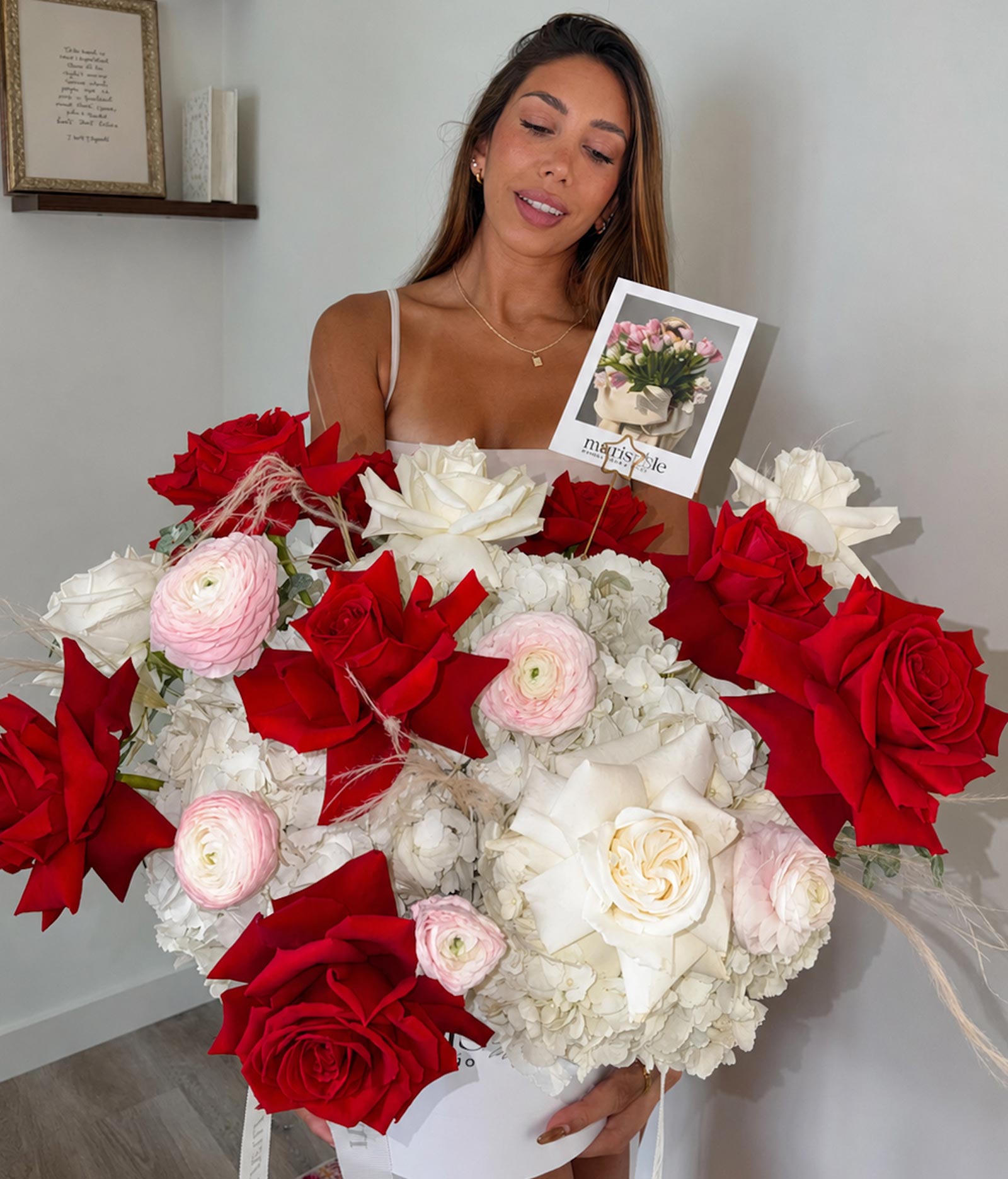 Woman holding a large bouquet of red, white, and pink flowers with a card in the background.