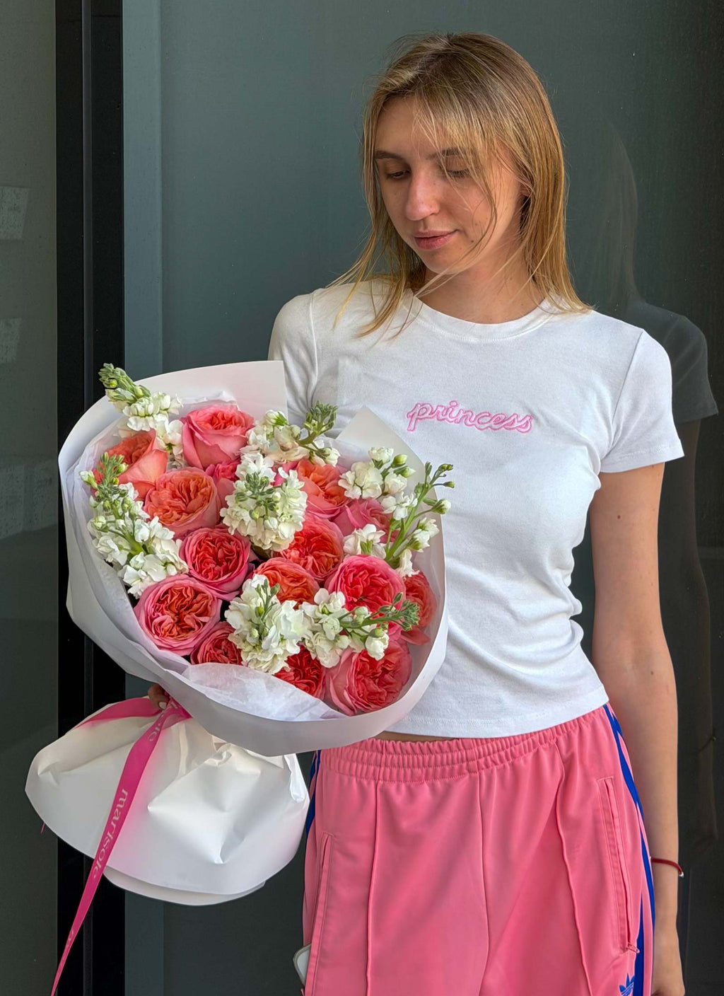 A woman holding a large bouquet of pink roses wrapped in white paper.