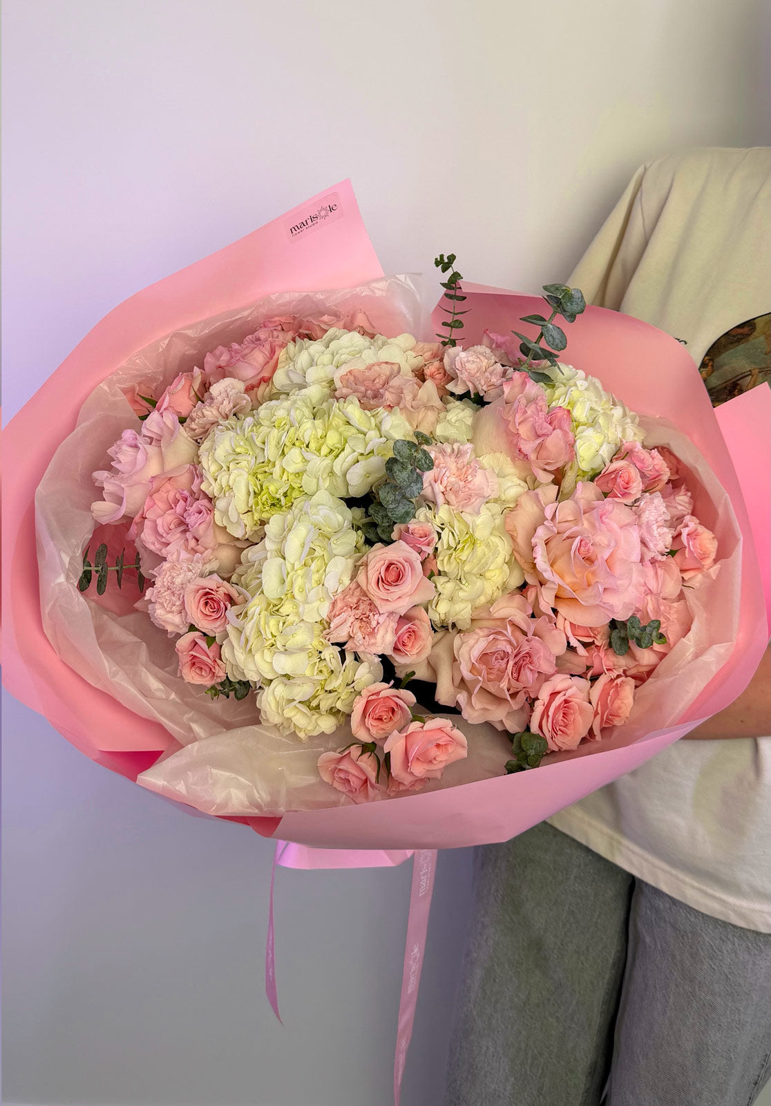 Bouquet of pink and white flowers wrapped in pink paper held by a person.