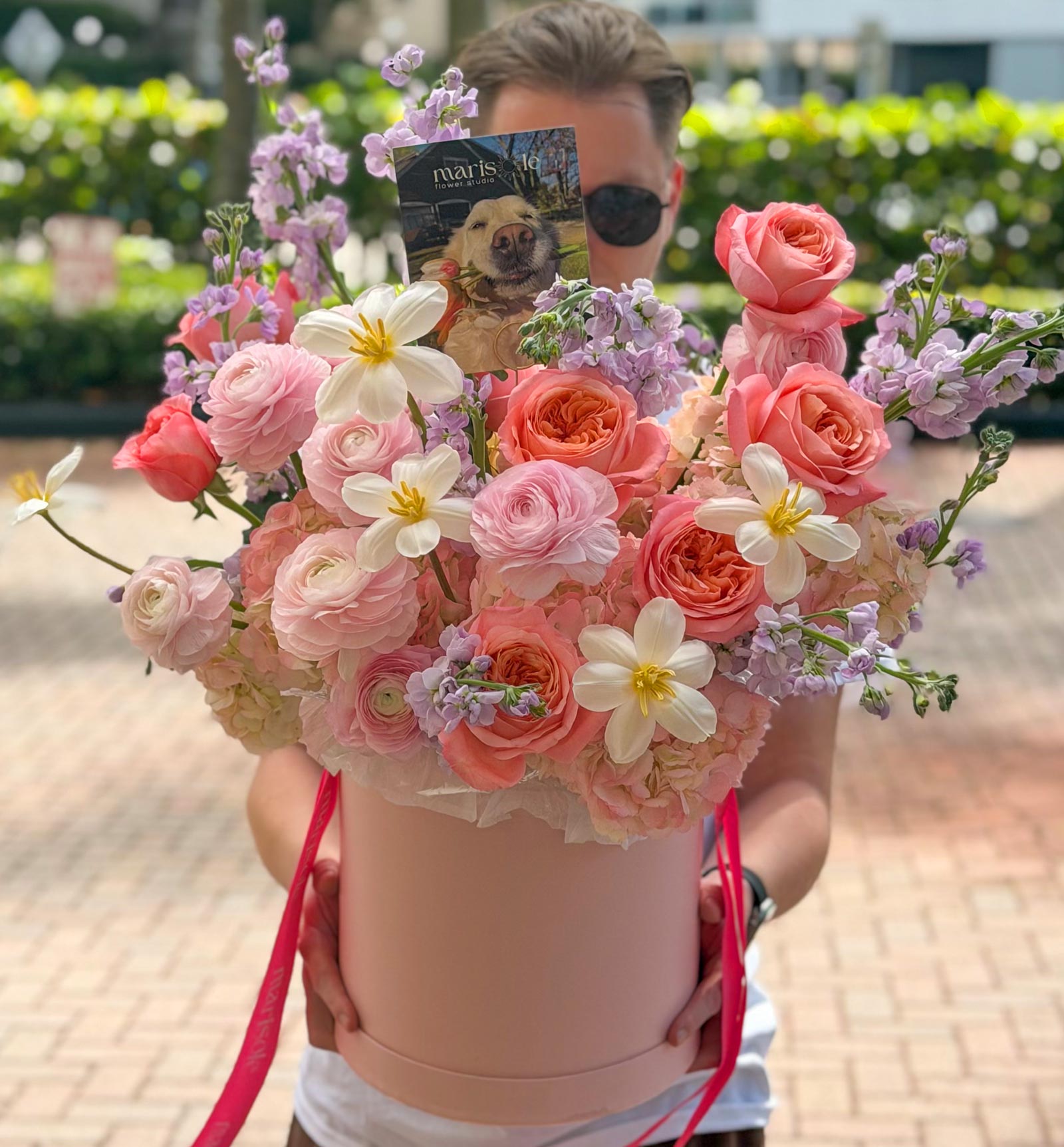 Person holding a bouquet of flowers in a pink box with a blurred background