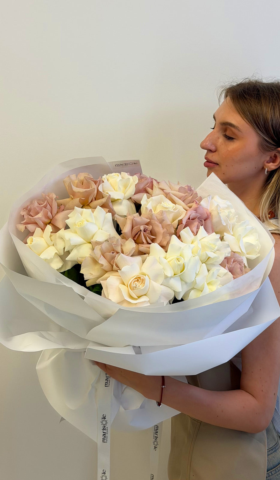 Person holding a large bouquet of flowers wrapped in white paper against a plain background