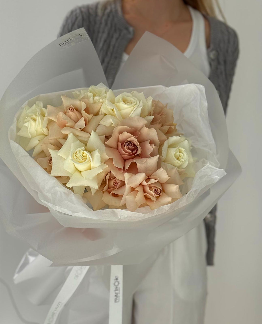 Bouquet of light-colored roses held by a person against a neutral background